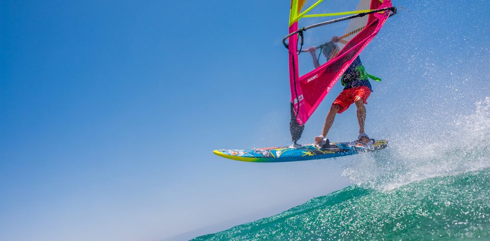 Young man jumping on waves with windsurfing board and colourful sail.